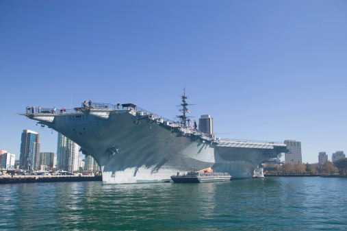 San Diego, United States of America - February 25, 2014: The historic aircraft carrier, USS Midway Museum moored in Broadway Pier in Downtown San Diego, Southern California, United States of America and the skyline. A battleship commissioned after the World War II.
