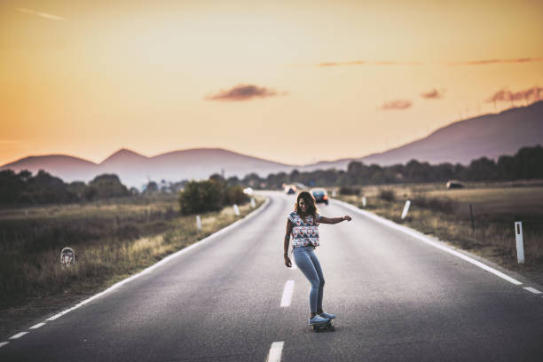 Full length of skilful woman skateboarding on an empty road in nature. Copy space.