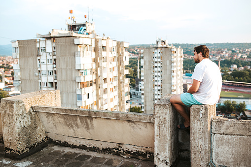 Young caucasian sad lonely man sitting on a high building rooftop.