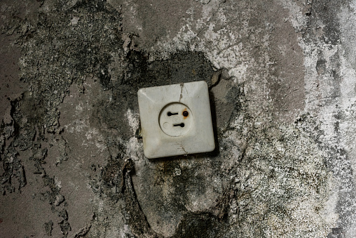 rusty power socket in damaged grey wall