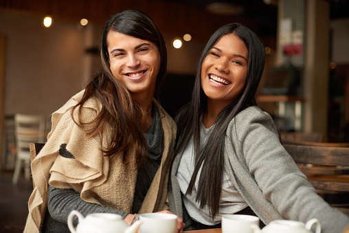 Cropped shot of two affectionate young friends smiling while sitting together in a coffee shop