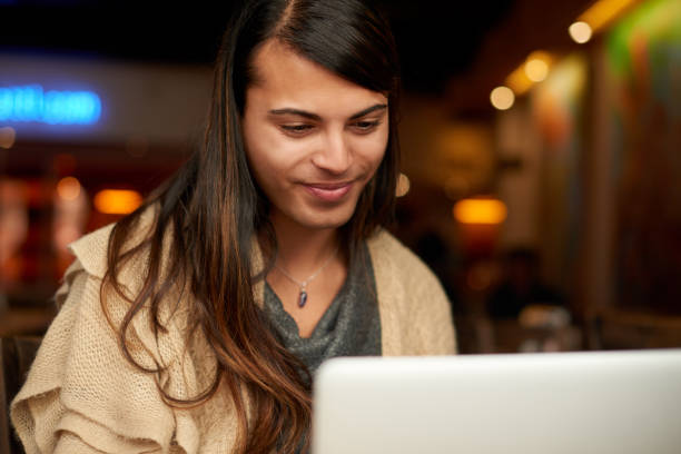 Everything looks good Cropped shot of a young gender fluid person smiling while using a laptop in a cafe gender fluid photos stock pictures, royalty-free photos & images