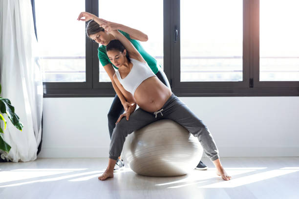 fisioterapeuta ayudando a la hermosa mujer embarazada para hacer ejercicios de pilates con pelota de preparación para el parto. - human pregnancy yoga exercising prenatal care fotografías e imágenes de stock