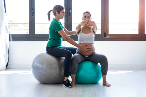 fisioterapeuta ayudando a la hermosa mujer embarazada para hacer ejercicios de pilates con pelota de preparación para el parto. - human pregnancy yoga exercising prenatal care fotografías e imágenes de stock