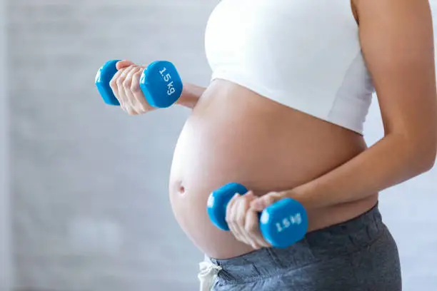 Close-up of pregnant woman doing exercise with dumbbells at home.