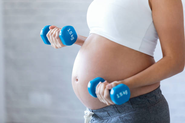 mulher gravida que faz o exercício com dumbbells em casa. - adult abdomen blue the human body - fotografias e filmes do acervo