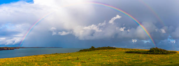 Moody sky with full rainbow bridge over british coast, South Wales,Uk.Bright and vibrant, panoramic coastline image.