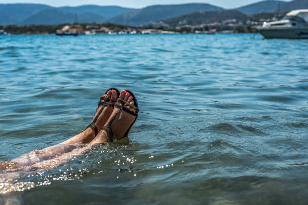 Female legs with sandals in the sea. Games with the sea. Summer day against the background of blue sky.
