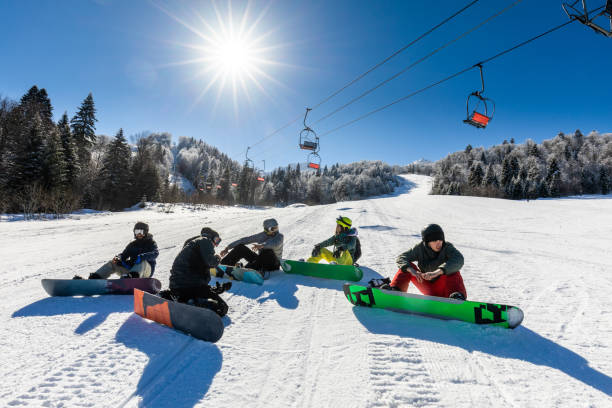 Group of young friends resting from snowboarding on mountain. Young happy friends talking while taking a break from snowboarding in winter day. Copy space. snowboarding snowboard women snow stock pictures, royalty-free photos & images