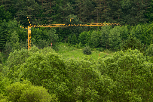 big yellow construction crane installed in the middle of the green forest