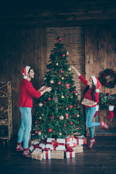 istock Vertical full length body size view of nice attractive cheerful cheery married spouses spending chistmastime having fun putting balls toys on fir in decorated loft industrial brick style interior 1177002432