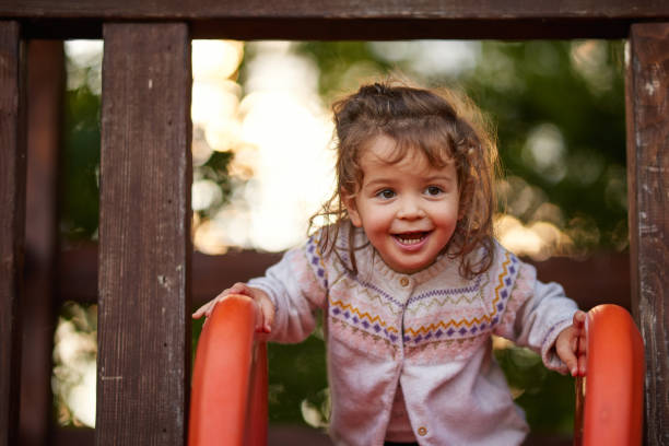Baby girl in the playground next to red slide, feeling happy