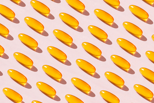 Abundance of yellow fish oil capsules repetition on soft pink background