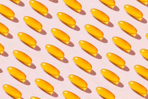 Soft Fish Oil Capsules on Pink Background Abundance of yellow fish oil capsules repetition on soft pink background omega 3 stock pictures, royalty-free photos & images