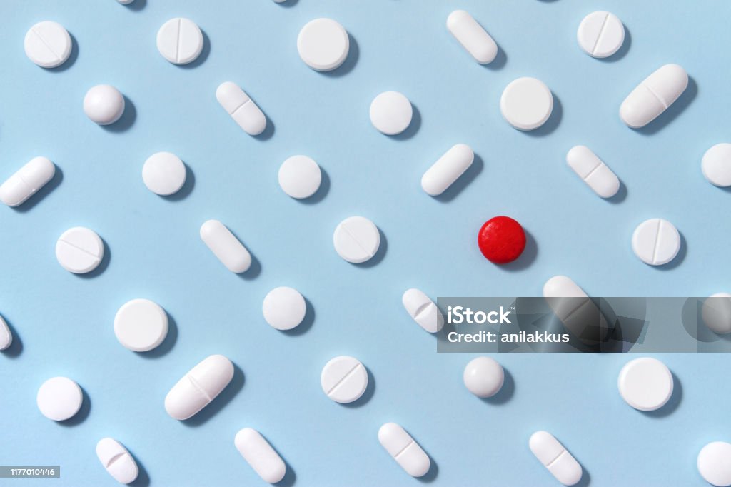 White Pills on Blue Background White pills arrangement on soft blue background with one red pill standing out from them Medicine Stock Photo