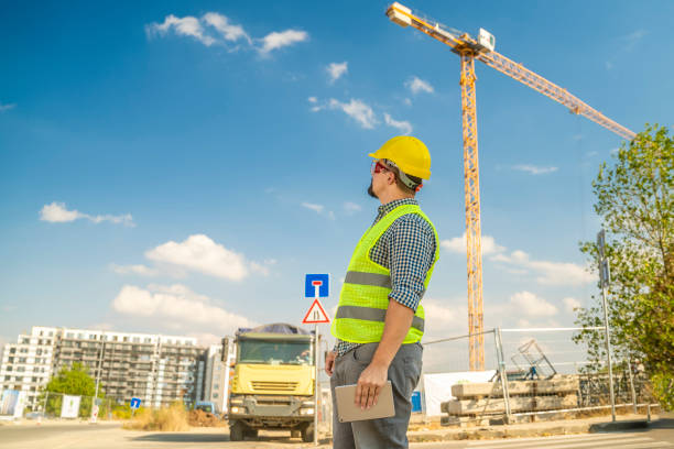 Architect, worker or construction engineer with tablet in front of truck and construction crane. The scene is situated outdoors in Sofia city industrial financial area during sunny summer day. The picture is taken with Sony A7III camera.