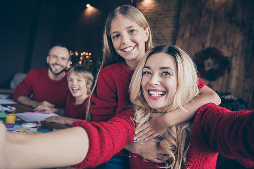 Closeup photo of dad mom and two children spending x-mas eve together, writing santa claus wish letter shooting funny selfies sitting table indoors wear red jumpers