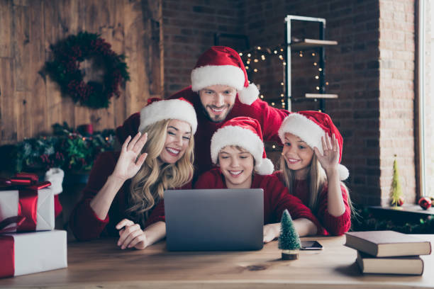 photo of dad mom and two children making x-mas eve skype video meeting conference waving arms congratulating relatives sitting table indoors wear red jumpers santa claus caps - vacations two generation family caucasian friendship imagens e fotografias de stock