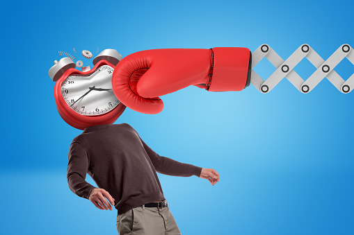 Huge red boxing glove punching man with an alarm clock instead of his face on blue background. Final deadline. Time expired. Time planning.