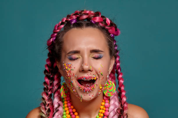 istock Lovely girl with a multi-colored braids hairstyle and bright make-up, posing in studio against a blue background. Colorful topping is on her face 1177016330