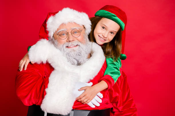빨간 배경 위에 고립 된 피기백을 껴안고 녹색 모자 모자에 안경 안경과 그의 엘프에 매력적인 크리스마스 아버지의 사진을 닫습니다 - glasses child red hair little girls 뉴스 사진 이미지