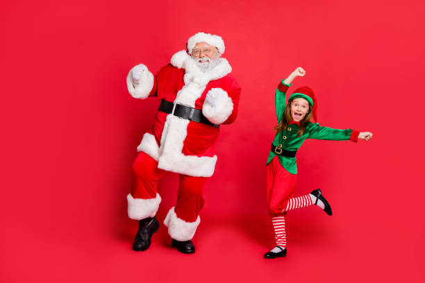 빨간 배경 위에 고립 된 녹색 밝은 의상을 입고 축제 행사에서 모자 모자 를 입고 춤을 추는 흥분 된 두 산타 클로스의 전신 사진 - glasses child red hair little girls 뉴스 사진 이미지