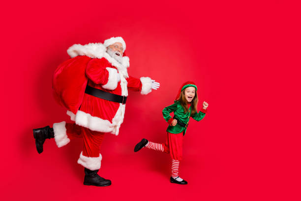 Full body profile side photo of cheerful two fairy runners santa claus elf  in hat headwear carrying heavy bag with presents on midnight wearing eyeglasses eyewear spectacles isolated over red background Full body profile side photo of cheerful two fairy runners santa claus elf  in hat headwear carrying heavy bag with presents on midnight wearing eyeglasses eyewear spectacles isolated over red background santa claus elf assistance christmas stock pictures, royalty-free photos & images