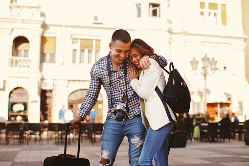 Happy young couple tourists walking in in the city and pulling suitcases and smiling