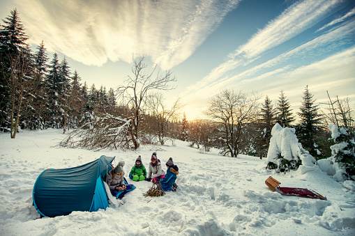 Family having fun playing in winter forest. Mother and kids are camping in the forest.\nNikon D850