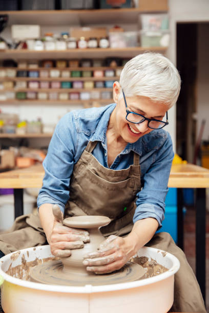 istock Senior female potter working on pottery wheel while sitting  in her workshop 1177025328