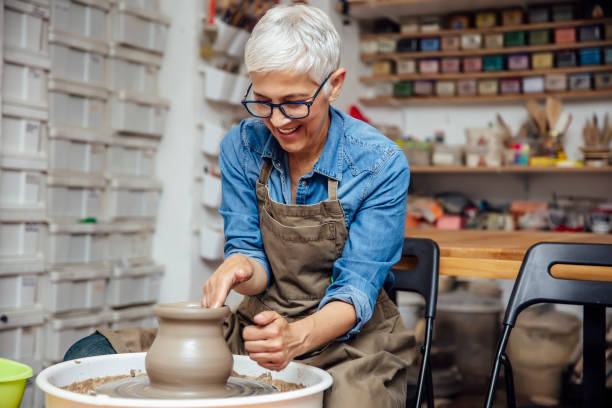 la alfarera mayor trabaja en la rueda de cerámica mientras está sentada en su taller - making craft craftsperson circle fotografías e imágenes de stock