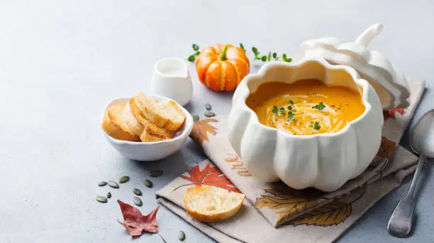 Photo of Pumpkin and carrot cream soup in bowl on grey stone background. Copy space.