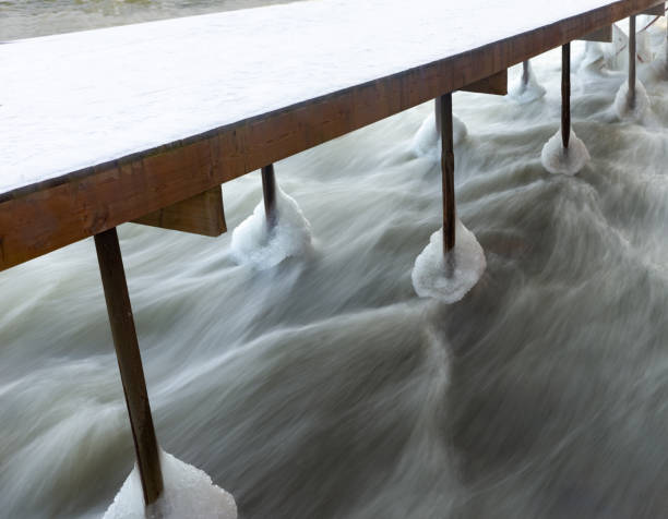 Wooden jetty on poles with ice in fast flowing water, long exposure.