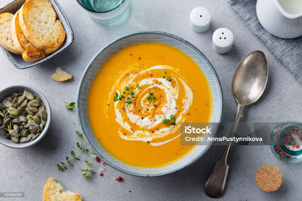 Pumpkin and carrot soup with cream on grey stone background. Top view. Pumpkin and carrot soup with cream on grey stone background. Top view Soup Stock Photo