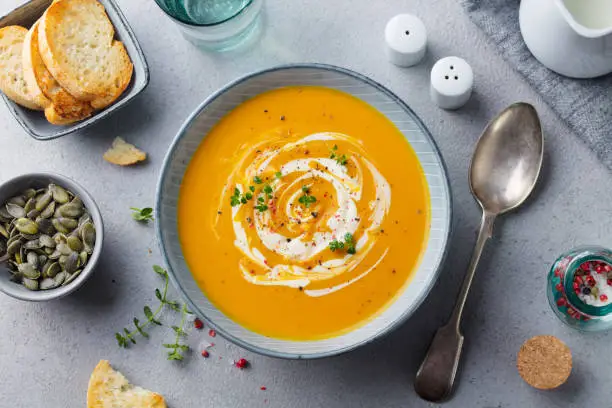Pumpkin and carrot soup with cream on grey stone background. Top view