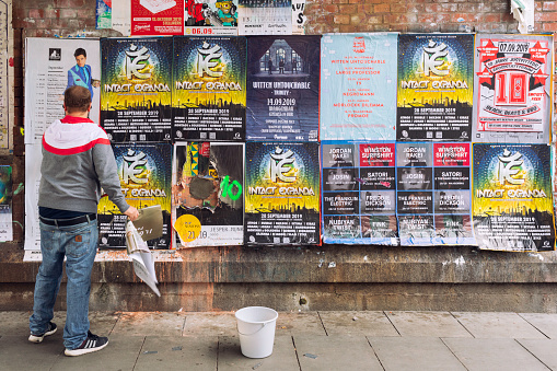 A man puts up new posters on a wall where many music and entertainment events are marketed.