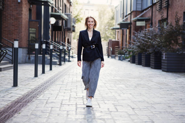 confident businesswoman or fashion blogger in stylish office clothes walking city street. . beautiful smiling woman going to work, wearing fashionable spring or fall black jacket, oversize slouchy jeans - fashion women posing looking at camera imagens e fotografias de stock