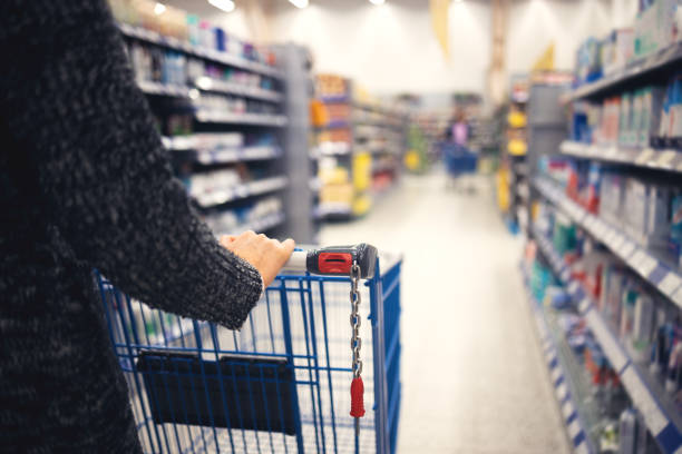 A women walks with a shopping basket in a store. Hand and part of the basket in focus stock photo