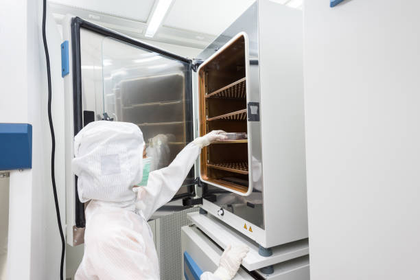 A scientist in sterile coverall gown placing cell culture flasks in the CO2 incubator. Cleanroom facility stock photo