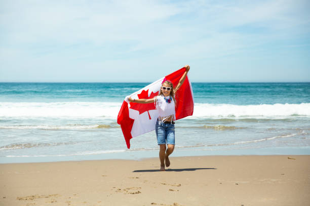 Happy Canadian girl carries fluttering white red flag of Canada against blue sky and ocean background. Happy Canadian girl carries fluttering white red flag of Canada against blue sky and ocean background. Canadian flag is a symbol of freedom, liberty, democracy, independence. Canada Day victoria day canada photos stock pictures, royalty-free photos & images