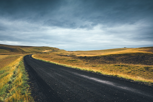 Black dirt road leading through Icelandic landscape.