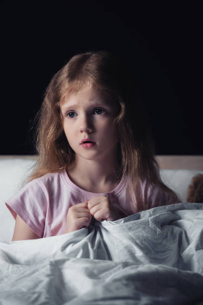 istock frightened kid looking away while sitting on bedding isolated on black 1177076501