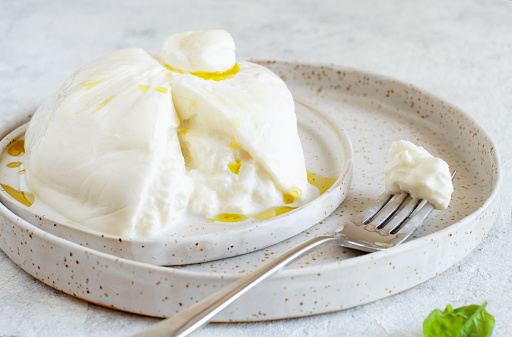 Italian cheese burrata on a plate with a fork and basil