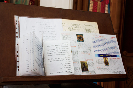 Various religious Scriptures lie on wooden stand for Bible in Church. Sacred Lectern for liturgy with open holy texts in Arabic on background of Church decoration.