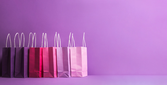 Paper shopping bags on a purple background. Christmas shopping concept. Xmas gifting context. Banner for shopping. Pink paper bags in a row.