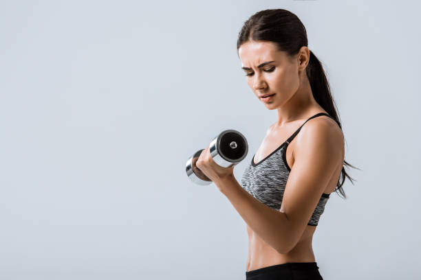 istock attractive brunette sportswoman using dumbbell isolated on grey 1177087749