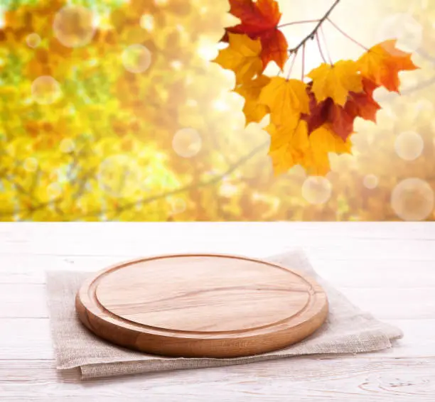 Photo of Pizza board with tableclothe on wooden desk. Autumn background. Top view mock up. Selective focus.
