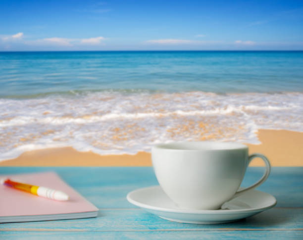 istock A cup of coffee and notebook with blurred beach sand and blue sky in day light 1177089125