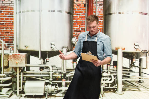 One person / one man only / waist up of 20-29 years old handsome people caucasian young men / male production line worker at the brewery / distillery / factory / food processing plant wearing button down shirt who is drunk / confusion / uncertainty who is working and holding alcohol / beer - alcohol / clipboard / barley / small business una persona / un hombre sólo / cintura para arriba de 20-29 años de edad personas hermosas hombres jóvenes caucásicos / trabajador de la línea de producción masculina en la cervecería / destilería / fábrica / planta de procesamiento de alimentos c
