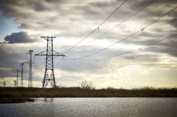 istock High voltage power tower pylon, lake water cloudy sky 1177096880